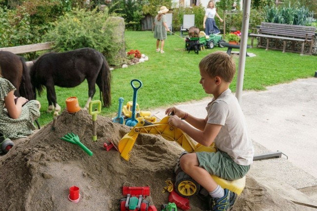 Kinder spielen in der Sandkiste am Linharterhof und genießen den Bauernhofurlaub in der Steiermark mit viel Platz zum Toben und Entdecken.