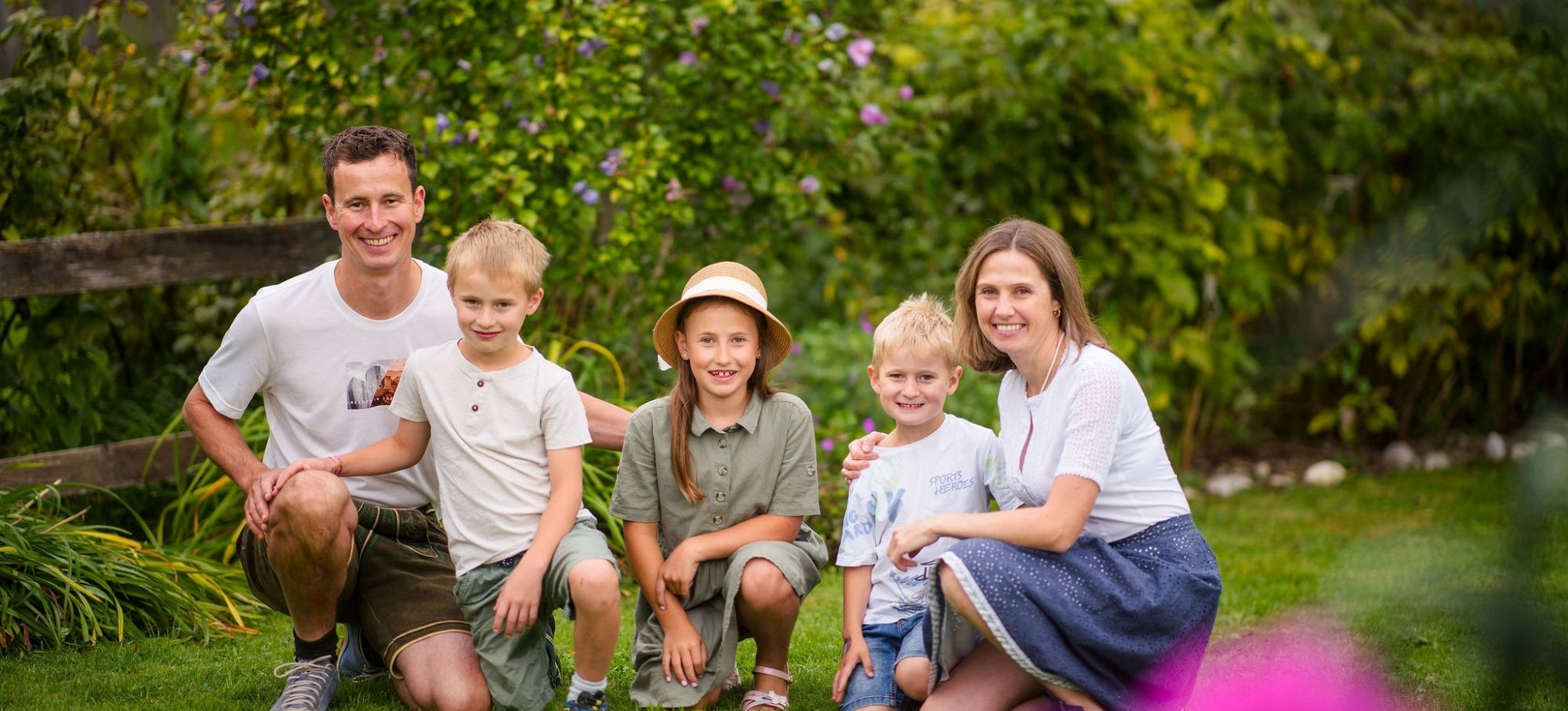 Eine lachende Familie Gruber im Garten, die herzlich willkommen heißt.